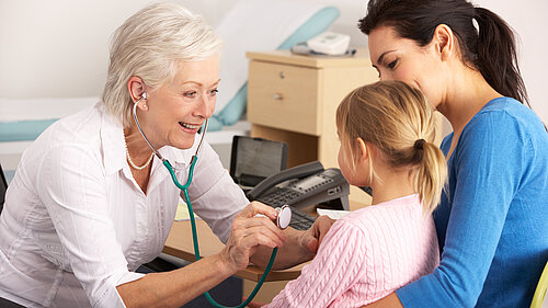 A mother holding a child whilst a GP checks on her using a stethoscope.